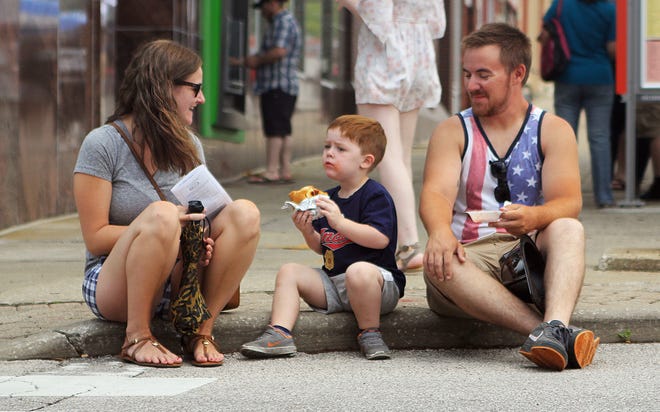Sarah Wick, son, Tanner Burbridge, 4, and Daniel Burbridge, of Stow, sit on the sidewalk while Tanner eats a calzone during the 2017 Heritage Festival in downtown Kent.