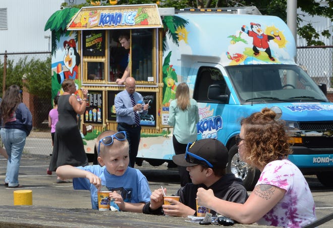 From left, Scott McCormick, 6, Eric Greene, 11, and Greene's mother Holly Geeting eat shaved ice from the Kona Ice truck (background) in Erie on June 25. [GREG WOHLFORD/ERIE TIMES-NEWS]