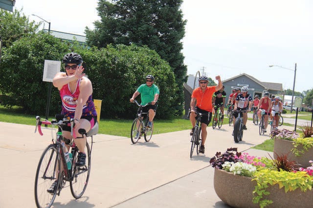 Riders wave as they make their way out of Perry on the Raccoon River Valley Trail as part of the BACooN Ride on Saturday, June 16. PHOTO BY ALLISON ULLMANN/THE PERRY CHIEF