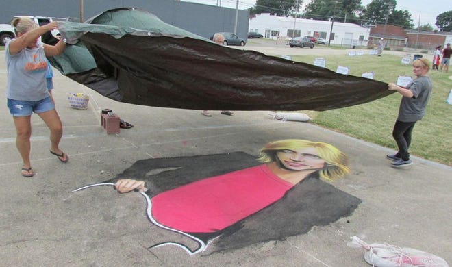 Heather Hoadley (above, right), of Kewanee, gets help placing a tarp on her Tom Petty chalk portrait before the rain came Friday night at the Kewanee Prairie Chicken Chalk Art Contest. Hoadley was the eventual champion of the event, with photos of entries taken for judging prior to the rain.