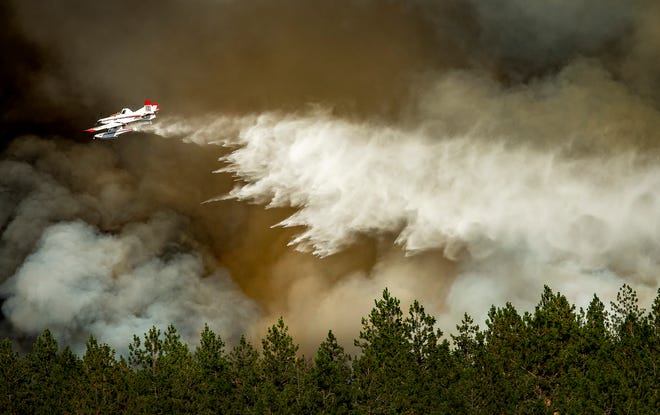 A firefighting aircraft makes a water drop on a wildfire approaching a house, Tuesday, July 17, 2018 in Spokane, Wash. Fire crews from Spokane, Spokane Valley and Fire District 9 are fighting a fast-moving wildfire just north of Upriver Drive that has engulfed several homes and prompted fire officials to call for a level three evacuation for homeowners in the area. (Colin Mulvany/The Spokesman-Review via AP)