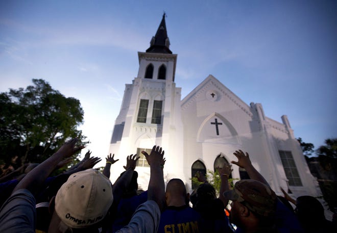 FILE - In this Friday, June 19, 2015, file photo, the men of Omega Psi Phi Fraternity Inc. lead a crowd of people in prayer outside the Emanuel AME Church, after a memorial service for the nine people killed by Dylann Roof in Charleston, S.C. The historic South Carolina church where nine black worshippers were slain is unveiling the design for a memorial to the victims. Emanuel AME Church in Charleston released the plans at an announcement Sunday, July 15, 2018, as part of its 200th anniversary celebration. The memorial was designed by Michael Arad, the architect behind the 9/11 Memorial in New York. [AP Photo/Stephen B. Morton, File]