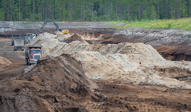 Dump trucks wait to be filled with sand from an excavator in a sand mine, off U.S. 1, north of St. Augustine on Monday. The mine fills more than 250 trucks a day with sand for area construction projects. [PETER WILLOTT/THE RECORD]