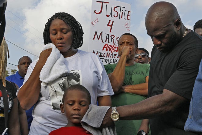 In this Sunday, July 22, 2018 photo, Michael McGlockton, right, the father of Markeis McGlockton, wipes the face of his grandson and five year-old-son of Markeis, Markeis McGlockton Jr., as protesters gathered to voice their concerns in Clearwater Fla. The family of McGlockton issued an appeal through their attorney for the public to put pressure on State Attorney Bernie McCabe to file charges against Michael Drejka, who fatally shot the father of three last Thursday during an argument over a handicapped parking space outside a convenience store. (Luis Santana/Tampa Bay Times via AP)