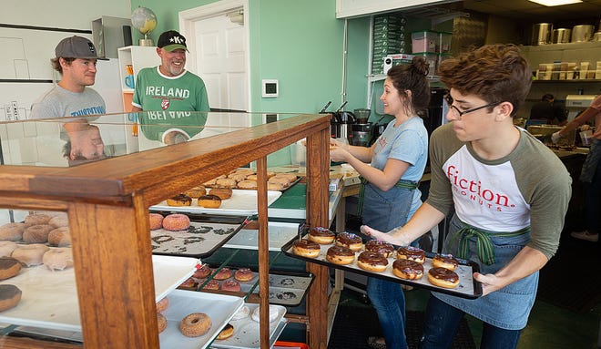 Fiction Donuts owner Danielle Broderson waits on a customer while Francis Wells restocks a display case with chocolate donuts on Friday. [PETER WILLOTT/THE RECORD]