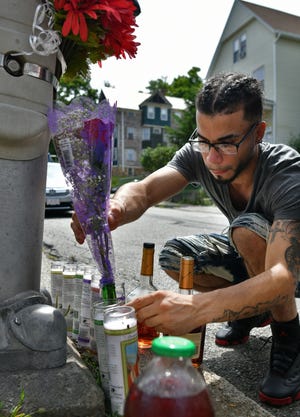 Alexander Burgos places roses in a bottle of water in memory of his friend who was shot on Sturgis Street early Sunday morning. Mr. Burgos and other friends set up a makeshift memorial in front of 11 Sturgis St. [T&G Staff/Christine Peterson]
