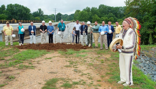 After placing again their shovels into the soil, members of the Wil-Cox Bridge steering committee listen as the Rev. Dr. Fleming 'Chief Holy Eagle' Otey blesses the ceremonial groundbreaking for the Wil-Cox Bridge site at the Yadkin River on Monday morning. The Wil-Cox Bridge will be the centerpiece of the project that also includes historic Fort York that overlooks the river. [Donnie Roberts/The Dispatch]