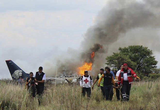 Red Cross workers and rescue workers carry an injured person on a stretcher, right, as airline workers, left, walk away from the site where an Aeromexico airliner crashed in a field near the airport in Durango, Mexico, Tuesday. [Red Cross Durango via AP]