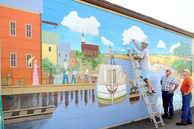 Port Washington resident Ed Steffek adds some finishing strokes to this large wall mural depicting the village in the late 1880's. So far, Ed said he has about 85 hours involved and hopes to finish in about a week. Located on the wall of Bates Metal Products, the mural of Lock 18 is something he wanted to do to give back to the community. Ed, who has been an artist for some 15 years, said he has done other murals but none outside. Also pictured is Jim Bates, center, owner of Bates Metal Products, and Port Washington Mayor Tom Gardner.