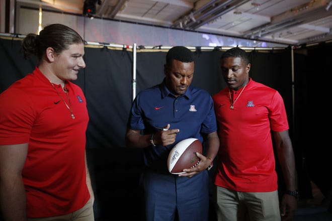 Flanked by linebacker Colin Schooler (left) and quarterback Khalil Tate (right), Arizona coach Kevin Sumlin as he signs an autograph at the Pac-12 Conference media day in Los Angeles last week. [AP Photo/Jae Hong]