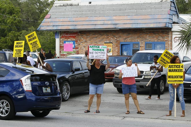 Friends and family of Markeis McGlockton hold up signs in a parking lot in Clearwater where he was shot and killed in an altercation. Michael Drejka, 47, fatally shot McGlockton on July 19 in a confrontation over a handicap-reserved parking space but has not been charged. [Luis Santana/Tampa Bay Times]