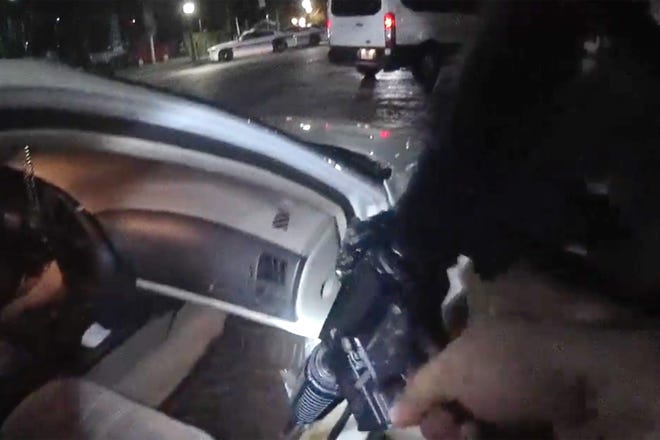 In this image from body cam video, a Gainesville police officer examines a Smith & Wesson AR 15 found on the backseat of a car in which two University of Florida football players were traveling. [GPD}