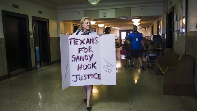 Kelly Jones, ex-wife of Alex Jones of Infowars, holds a protest sign as she walks down the hall outside a Travis County state District Court on Wednesday. Lawyers for Mr. Jones are seeking to dismiss a defamation lawsuit at a hearing held at the courthouse Wednesday, brought against him by the parents of a child slain at Sandy Hook Elementary School in 2012. The parents say Jones’ claims that the shooting was a hoax, has turned their lives into a nightmare of abuse from his listeners.