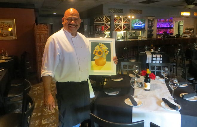 Girasoles chef and owner Jose Zambrano holds one of the paintings that the members of WOW put on exhibit. [Wayne Ford/Athens Banner-Herald]