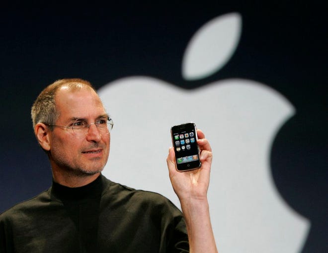 FILE - In this Jan. 9, 2007 file photo, Apple CEO Steve Jobs holds up the new iPhone during his keynote address at MacWorld Conference & Expo in San Francisco. Apple has become the worldâ€™s first company to be valued at $1 trillion, the financial fruit of tasteful technology that has redefined society since two mavericks named Steve started the company 42 years ago. (AP Photo/Paul Sakuma, File)