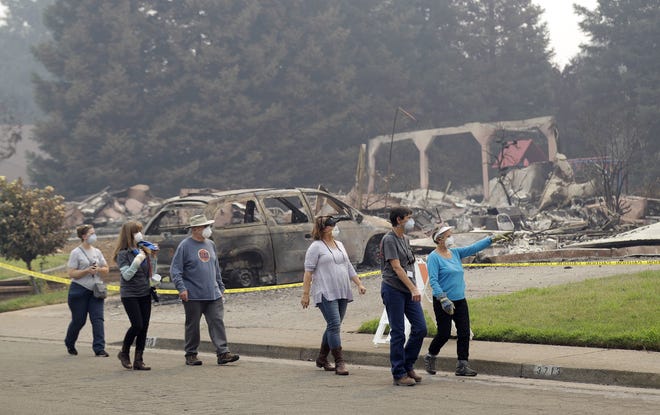 CORRECTS TO SUZIE SCATENA FROM SUZIE SCALENE - Carol Smith, far right in blue, her daughter Suzie Scatena, third from right, and husband Tim, third from left, tour their fire-ravaged neighborhood along with support crews Thursday, Aug. 2, 2018, in Redding, Calif. The Smith's home of 30 years was destroyed by a wildfire. (AP Photo/Marcio Jose Sanchez)