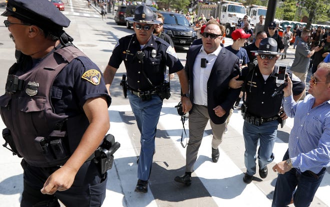 FILE - In this Tuesday, July 19, 2016 file photo, Alex Jones, center right, is escorted by police out of a crowd of protesters outside the Republican convention in Cleveland. Facebook says it has taken down four pages belonging to conspiracy theorist Alex Jones for violating its hate speech and bullying policies. The social media giant said in a statement Monday, Aug. 6, 2018 that it also blocked Jones' account for 30 days because he repeatedly posted content that broke its rules. (AP Photo/John Minchillo, File)