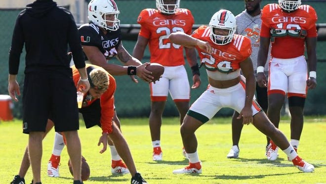 Hurricanes quarterback Malik Rosier hands off the ball to running back Travis Homer during football practice at the Greentree Practice Field on Monday, August 6, 2018.
