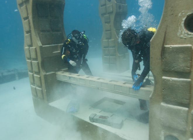 In this July 19, 2018 photo, Jim Hutslar, right, operations director for Neptune Memorial Reef, and Ray Lowenstein, left, prepare to install a memorial plaque for Buel and Linda Payne, affixed to at cement baluster mixed with their ashes, at the Neptune Memorial Reef near Miami Beach, Fla. The Paynes are the first to be memorialized in the reef's expansion which started this summer and will make room for an additional 4,000 memorials. (AP Photo/Wilfredo Lee)