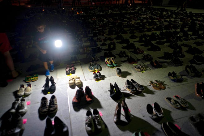 A child shines a light on hundreds of shoes at a memorial for those killed by Hurricane Maria in front of the Puerto Rico Capitol in San Juan. Puerto Rico has conceded that Hurricane Maria killed more than 1,400 people on the island last year and not just the 64 in the official death toll. [Ramon Espinosa/The Associated Press]