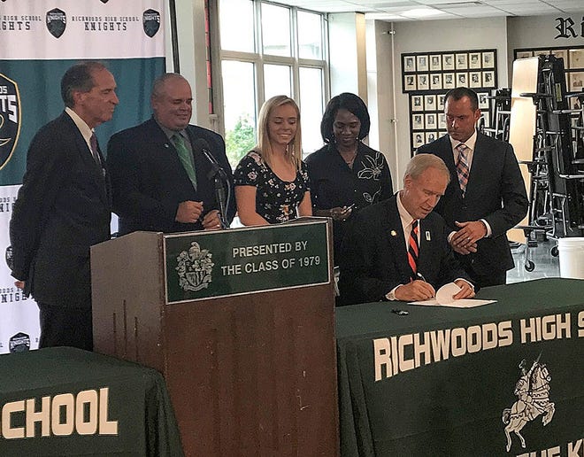 Gov. Bruce Rauner signs a bill lifting limits on dual credit courses Friday as state Sen. Chuck Weaver, from left, Rep. Dan Swanson, Richwoods High School senior Mckenna Myers, Peoria Public Schools Superintendent Sharon Desmoulin-Kherat and Richwoods Principal Brett Elliott look on. [SUBMITTED PHOTO]