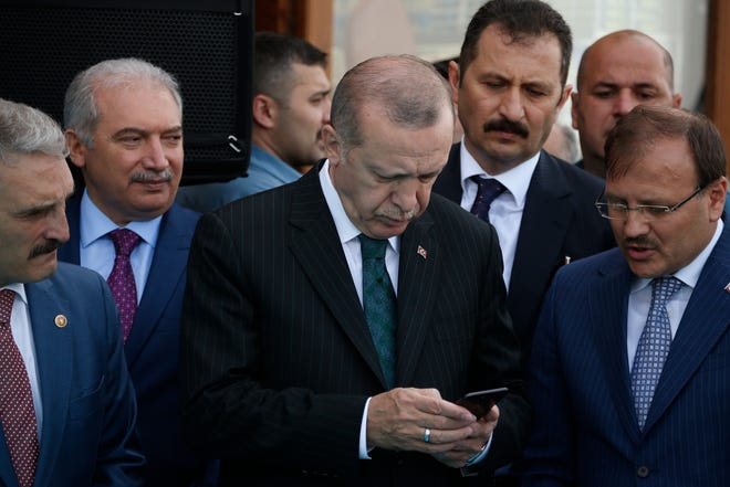 FILE - In this Friday, May 4, 2018 file photo, Turkey's President Recep Tayyip Erdogan, center, looks at his phone during a ceremony in Istanbul. Erdogan said Tuesday, Aug. 18, 2018, that his country will boycott U.S.-made electronic goods amid a diplomatic spat that has helped trigger a Turkish currency crisis. Showing no signs of backing down in the standoff, Erdogan suggested that Turkey would stop procuring U.S.-made Iphones and buy Korean Samsung or Turkish-made Vestel instead. (AP Photo/Lefteris Pitarakis, File)