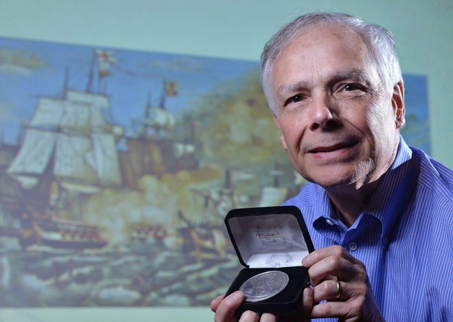 Chris Baldwin with a medal honoring an officer who fought in the Battle of Lake Erie, an artist's rendering of which is projected in the background. [CHRISTOPHER MILLETTE FILE PHOTO/ERIE TIMES-NEWS]