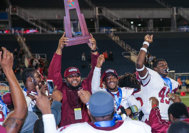 Raines head coach Deran Wiley raises the trophy as team celebrates winning the 4A state championship against Cocoa 13-10 on Dec. 7, 2017 in Orlando. [For The Florida Times-Union/Gary Lloyd McCullough]