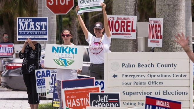 WEST PALM BEACH — Volunteers hold up signs outside the Palm Beach County Supervisor of Elections office Monday, August 13, 2018, as a people slowly straggled in to cast their votes throughout the afternoon. (Damon Higgins / The Palm Beach Post)