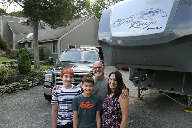 Eric and Leslie Lawton with their two sons, Oliver, 13, left, and Charlie, 12, stand beside their truck and trailer. The family is selling their North Kingstown home and gave away or sold nearly everything in it to pursue their transcontinental quest. [The Providence Journal / Bob Breidenbach]