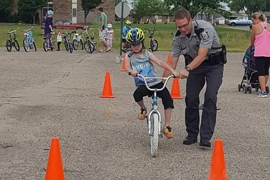 South Hutchinson Police Officer Keith Zerger assists with a bicycle rodeo in South Hutchinson in this file photo. The deparmtent has started a GoFundMe page to assist two officers, including Zerger, and a clerk being layed off. [Courtesy South Hutchinson Police]