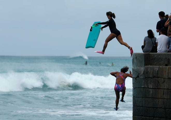 Bodyboarders jump into the surf along Waikiki Beach ahead of Hurricane Lane, Friday, Aug. 24, 2018, in Honolulu. (AP Photo/John Locher)