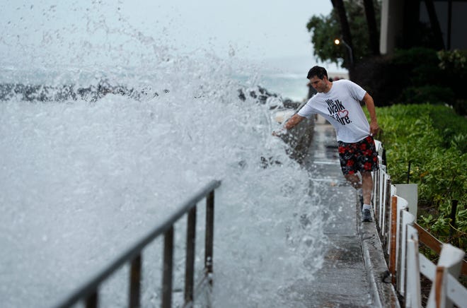 A man avoids getting splashed by a large wave on a walkway along a beach ahead of Hurricane Lane, Thursday, Aug. 23, 2018, in Honolulu. (AP Photo/John Locher)