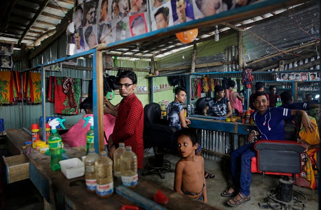In this Thursday, Aug. 23, 2018 photo, Rohingya refugees sit inside a newly setup barber shop at Kutupalong refugee camp, Bangladesh. A year after they were set up, the sprawling camps have become fully functional in Cox's Bazar district with new shops, roadside restaurants and medicine stores cropping up. Despite months of discussions among Myanmar, Bangladesh, the United Nations and a string of aid agences, there are few signs that the Rohingya can go home anytime soon. (AP Photo/Altaf Qadri)