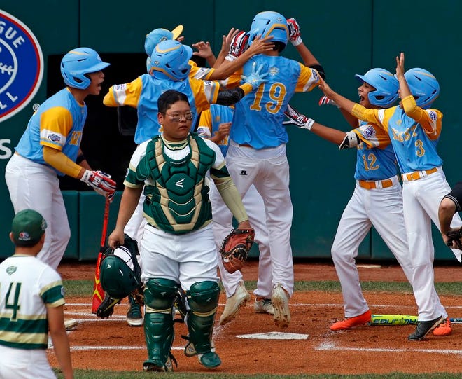 Hawaii's Mana Lau Kong (19) is greeted by teammates after hitting the first pitch from South Korea's Yeong Hyeon Kim, lower left, for a solo home run in the first inning of the Little League World Series Championship.
