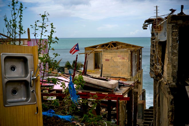 In this Oct. 5, 2017 file photo, a Puerto Rican national flag is mounted on debris of a damaged home in the aftermath of Hurricane Maria in the seaside slum La Perla, San Juan, Puerto Rico. An independent investigation ordered by Puerto Rico’s government estimates that nearly 3,000 people died as a result of Hurricane Maria. The findings issued Tuesday, Aug. 28, 2018, by the Milken Institute School of Public Health at George Washington University contrast sharply with the official death toll of 64. (AP Photo/Ramon Espinosa)