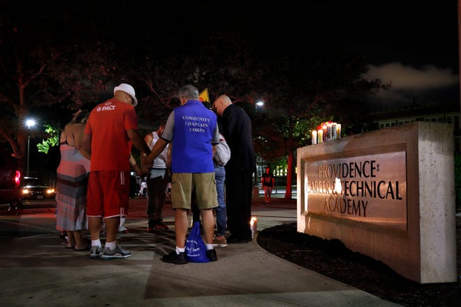 Members of the community pray Wednesday night in front of the Providence Career and Technical Academy sign where the 15-year-old Central High student was shot and killed earlier in the day. [The Providence Journal / Kris Craig]