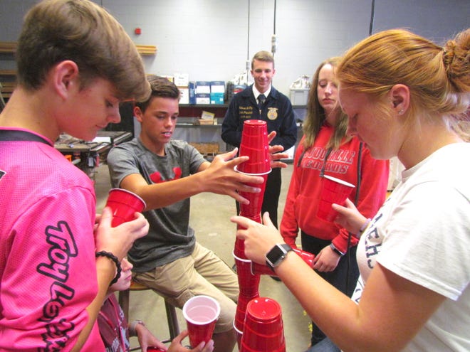 State FFA President Colesen McCoy watches Loudonville High School animal science students do a team-building activity during his visit to the school recently. They students were loosely tied together in groups of four and had to take cups and stack them as high as they could without knocking them over.