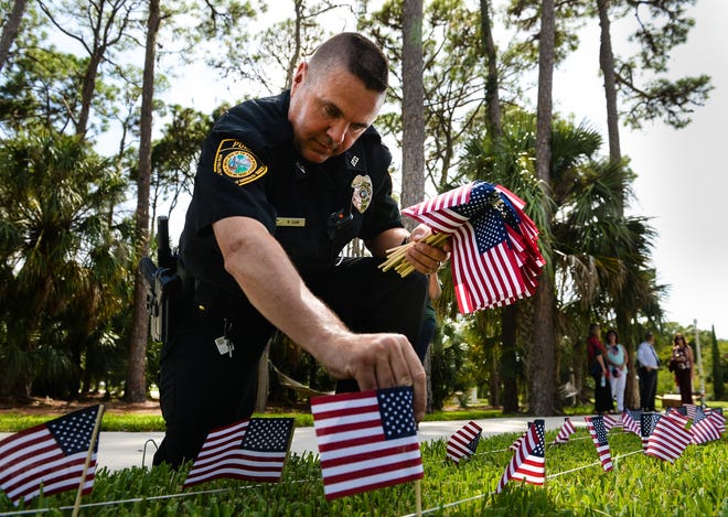 New College of Florida police officer Micheal Clary places American flags on the University of Sarasota Sarasota-Manatee campus lawn on Monday. Students, first responders, veterans and volunteers joined together to plant 2,977 small flags, one for each victim of the 9/11 attacks. USF Sarasota-Manatee will hold a 9/11 remembrance ceremony on Tuesday. [Herald-Tribune staff photo / Dan Wagner]