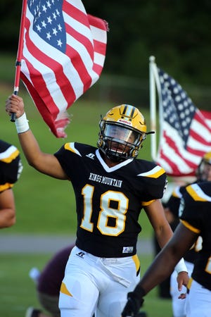 Kings Mountain's Titus Clark carries the American flag entering John Gamble Stadium for Kings Mountain's Aug. 24 season-opening win over South Caldwell. [Brittany Randolph/The Star]