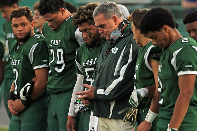 Cranston East head coach Tom Centore, center, and his players bow their heads before Friday night's game during a moment of silence fot Centore's father, former Johnston coach Tony Centore, who died Sept. 8.