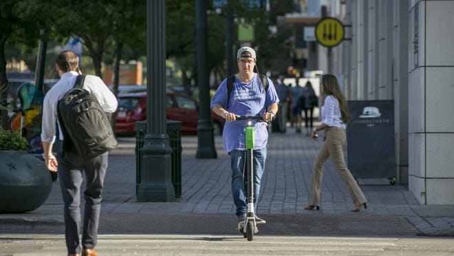 Pedestrians and a scooter rider share a sidewalk Wednesday at Congress Avenue and East Fourth Street. City code currently treats scooters as bicycles, allowing riders to use them in the street and on some sidewalks. JAY JANNER / AMERICAN-STATESMAN