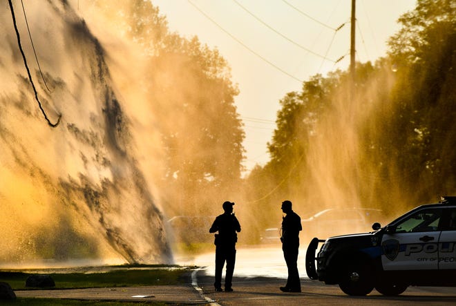 RON JOHNSON/JOURNAL STAR A water-main break in the 3000 block of West Lake Avenue sends a geyser of water 50 feet skyward as Peoria policemen keep traffic from crossing the road late Thursday afternoon.