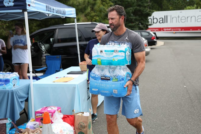 North Carolina football coach Larry Fedora carries two cases to water to a truck for transportation. [Kimberly Rivers, UNC Athletics]
