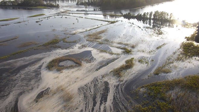 In this image made from drone video provided by the N.C. Department of Environmental Quality, light gray material flows out of a flooded coal ash dump toward the Cape Fear River at Duke Energy's L.V. Sutton Power Station in Wilmington, N.C. [N.C. Department of Environmental Quality via AP]