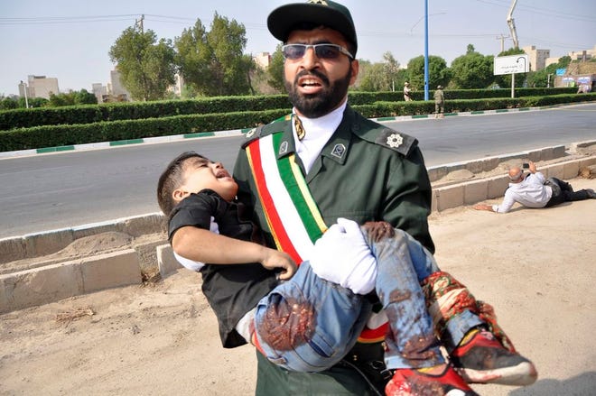 In this photo provided by the Iranian Students' News Agency, ISNA, a Revolutionary Guard member carries a wounded boy after a shooting during a military parade marking the 38th anniversary of Iraq's 1980 invasion of Iran, in the southwestern city of Ahvaz, Iran, Saturday, Sept. 22, 2018.