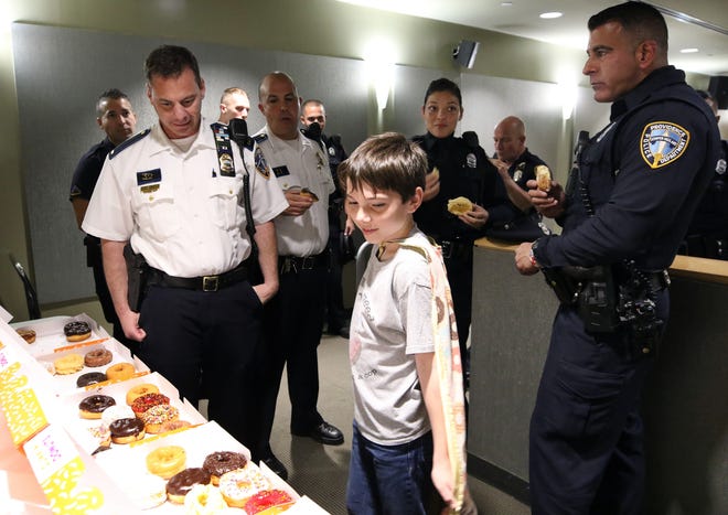 Ten-year-old Tyler Carach selects a doughnut for Providence Police Lt. Stephen Gencarella, left, as other officers enjoy their doughnuts after roll call on Monday. The Florida boy is traveling around the country delivering doughnuts to police officers as a way of saying thanks for their service. [The Providence Journal / Bob Breidenbach]