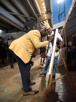 Hall of Fame Gold Jacket, Will Shields, signs a painting created by artist, Todd V., live on the stage during the event.