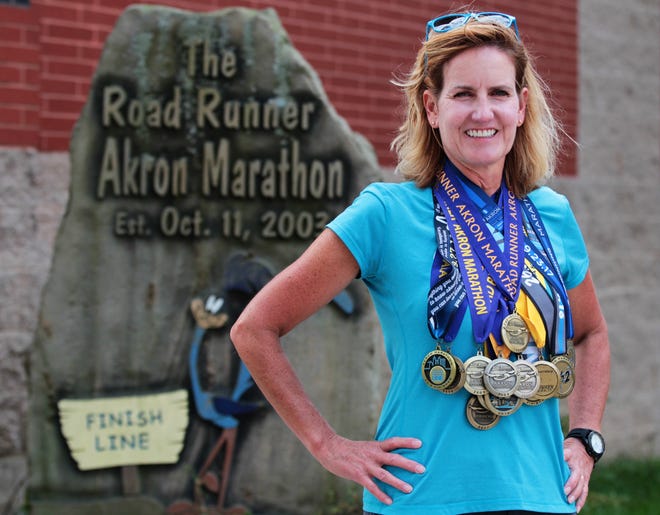 Melissa Johnson, 50 of Canton, wears the 14 medals she has from running every Akron marathon since the first one in 2003 near the Akron Marathon Finish line on Friday, Sept. 21, 2018 in Akron, Ohio. Johnson who has run in 99 marathons since her first Akron Marathon will make the 15th Akron Marathon her 100th total. [Mike Cardew/BeaconJournal/Ohio.com]