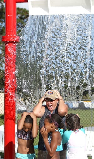 Mayor Margo Anderson stands under a bucket of water with children. The Leon Miller Splash Pad officially opened on Monday at Cain-Griffin Park in Lynn Haven. [PATTI BLAKE/THE NEWS HERALD]